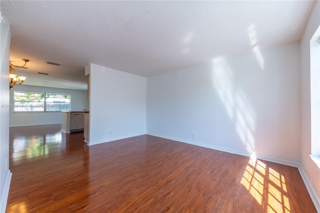 empty room with a chandelier, dark wood finished floors, a textured ceiling, and baseboards