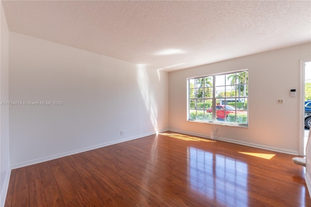 empty room with a textured ceiling, wood finished floors, and baseboards