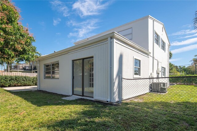 back of property featuring central AC unit, a lawn, and fence