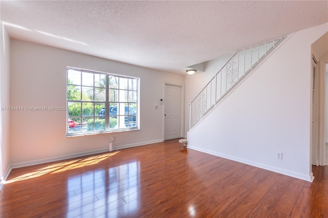 interior space featuring stairway, wood-type flooring, a textured ceiling, and baseboards