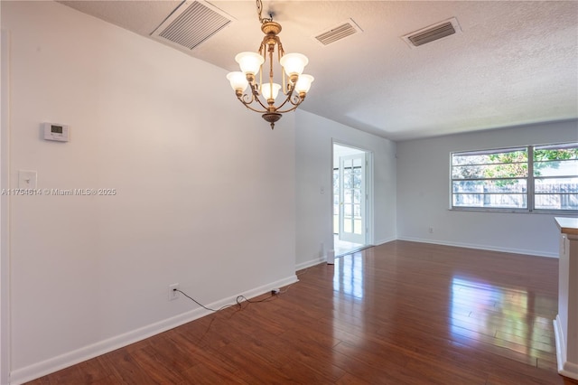 empty room featuring dark wood-style flooring, a chandelier, and visible vents