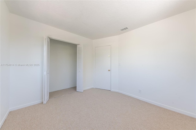 unfurnished bedroom featuring light carpet, baseboards, visible vents, a textured ceiling, and a closet