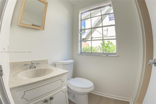 half bath featuring baseboards, vanity, toilet, and wood finished floors