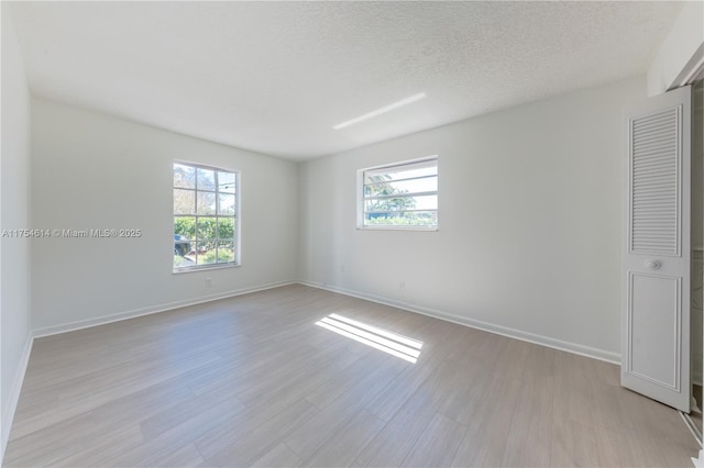 empty room with baseboards, light wood-type flooring, and a textured ceiling