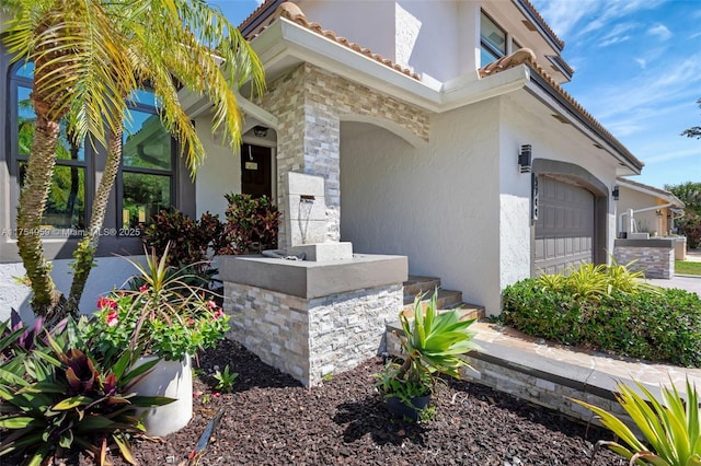 exterior space featuring a garage, a tiled roof, stone siding, and stucco siding