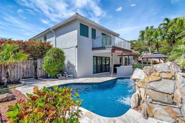 rear view of house with a fenced in pool, stucco siding, a patio area, fence, and a balcony