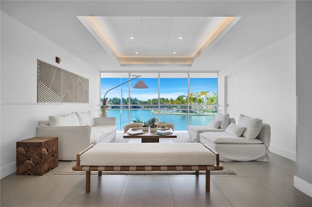 living room featuring recessed lighting, a water view, baseboards, expansive windows, and a tray ceiling