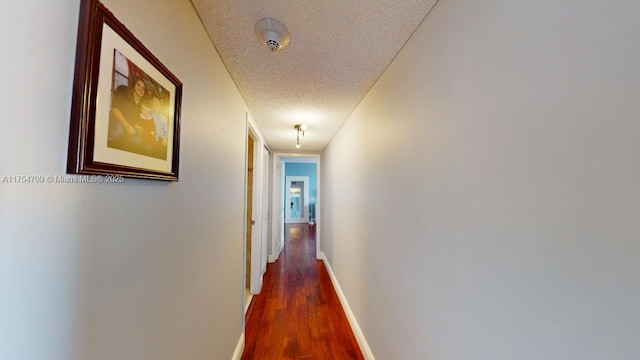 hall featuring dark wood-style floors, a textured ceiling, and baseboards