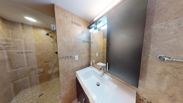 full bath with a tile shower, tile walls, and vanity