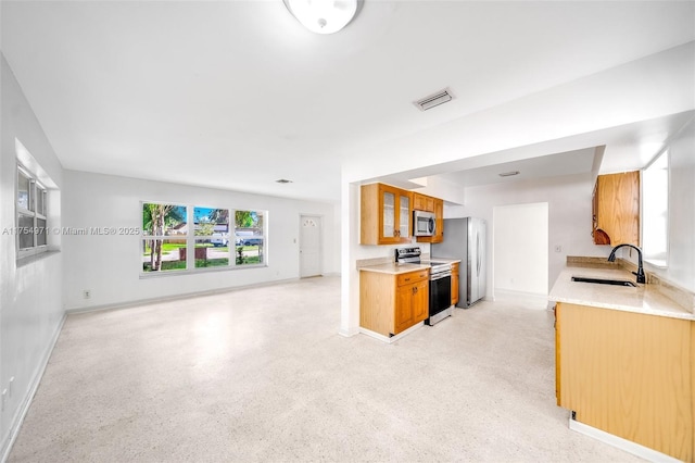 kitchen with visible vents, brown cabinetry, open floor plan, stainless steel appliances, and a sink