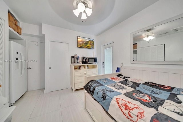 bedroom with light tile patterned floors, ceiling fan, white refrigerator with ice dispenser, and wainscoting