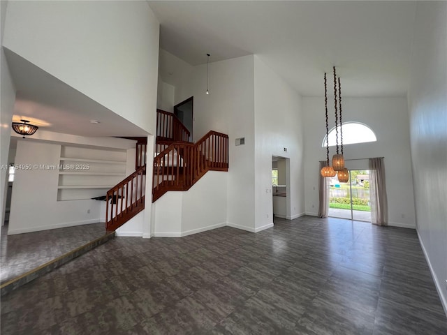 unfurnished living room featuring visible vents, stairway, a towering ceiling, and baseboards