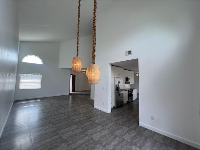 unfurnished living room featuring visible vents, a towering ceiling, and baseboards