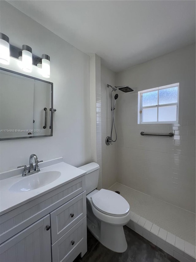 full bathroom with toilet, a tile shower, and vanity