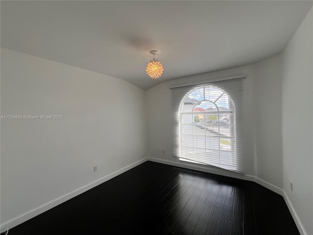 spare room with dark wood-style flooring, vaulted ceiling, and baseboards