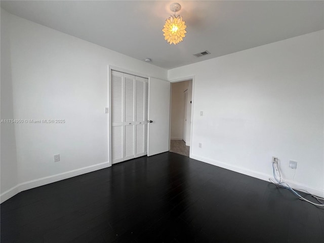 unfurnished bedroom featuring dark wood-style flooring, a closet, visible vents, and baseboards