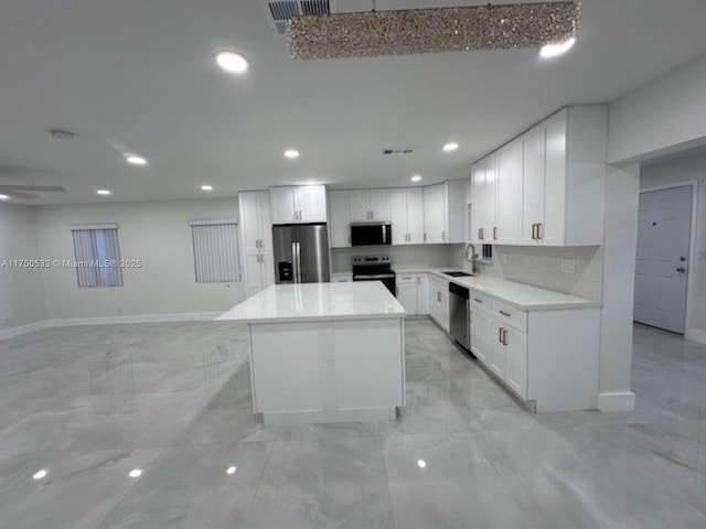 kitchen with a center island, stainless steel appliances, light countertops, white cabinets, and a sink