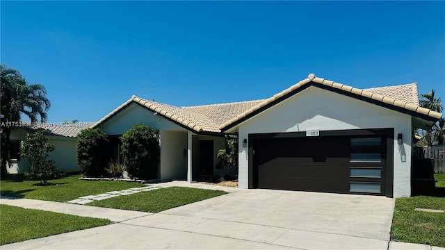 ranch-style house featuring a front yard, a tiled roof, an attached garage, concrete driveway, and stucco siding