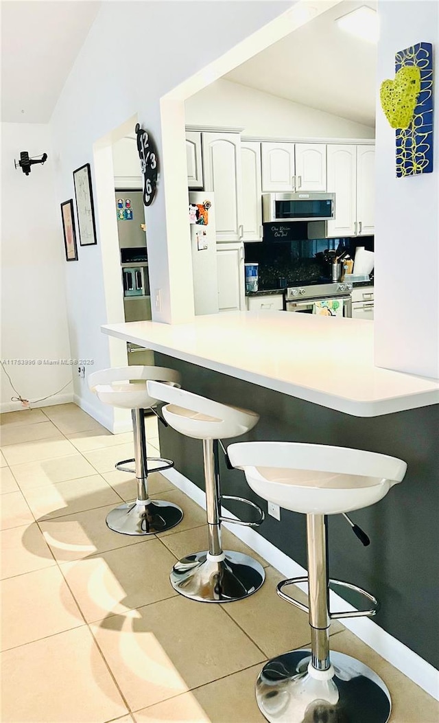 kitchen featuring light tile patterned floors, appliances with stainless steel finishes, a kitchen breakfast bar, white cabinetry, and lofted ceiling