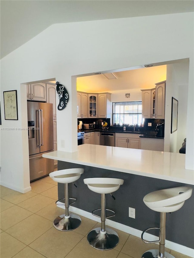 kitchen with baseboards, vaulted ceiling, glass insert cabinets, a breakfast bar area, and stainless steel appliances