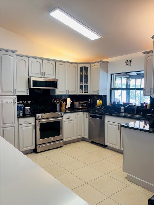 kitchen featuring dark countertops, light tile patterned floors, backsplash, and appliances with stainless steel finishes