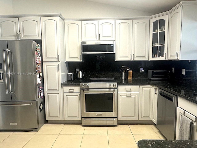 kitchen with glass insert cabinets, vaulted ceiling, appliances with stainless steel finishes, light tile patterned flooring, and a toaster