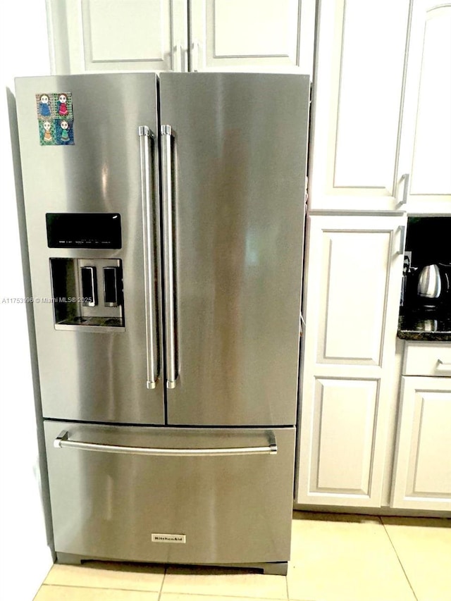 details with dark stone counters, stainless steel fridge, and white cabinets