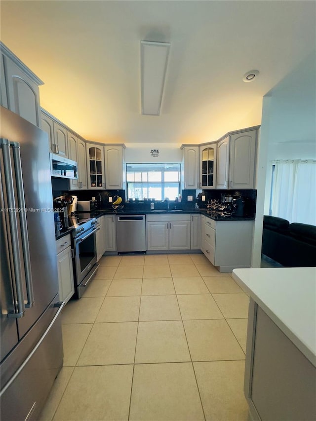 kitchen featuring light tile patterned floors, glass insert cabinets, a sink, stainless steel appliances, and backsplash