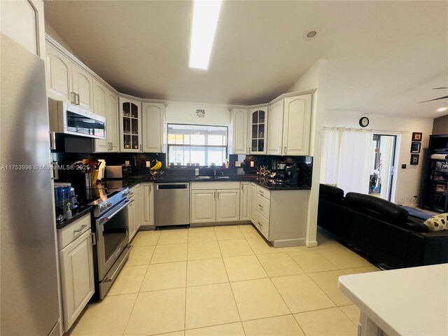 kitchen with dark countertops, glass insert cabinets, tasteful backsplash, and appliances with stainless steel finishes