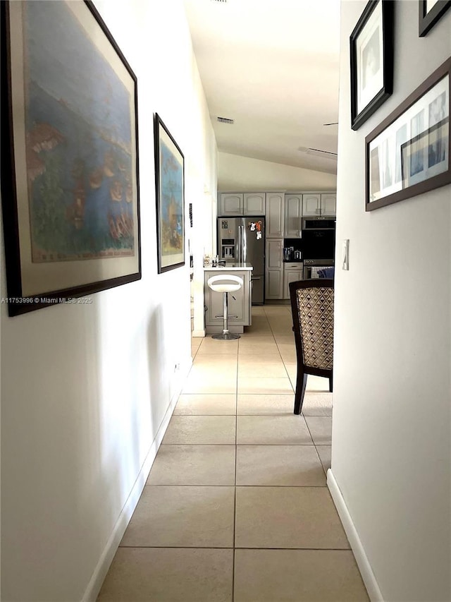corridor featuring light tile patterned floors, visible vents, baseboards, and lofted ceiling