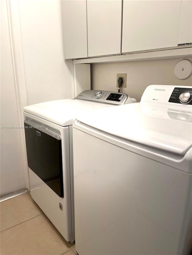 laundry area featuring light tile patterned floors, washing machine and clothes dryer, and cabinet space