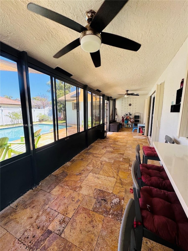 sunroom / solarium with a textured ceiling, a ceiling fan, and stone tile flooring