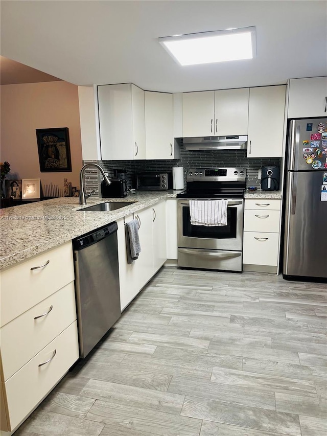 kitchen featuring stainless steel appliances, tasteful backsplash, light wood-style flooring, a sink, and under cabinet range hood