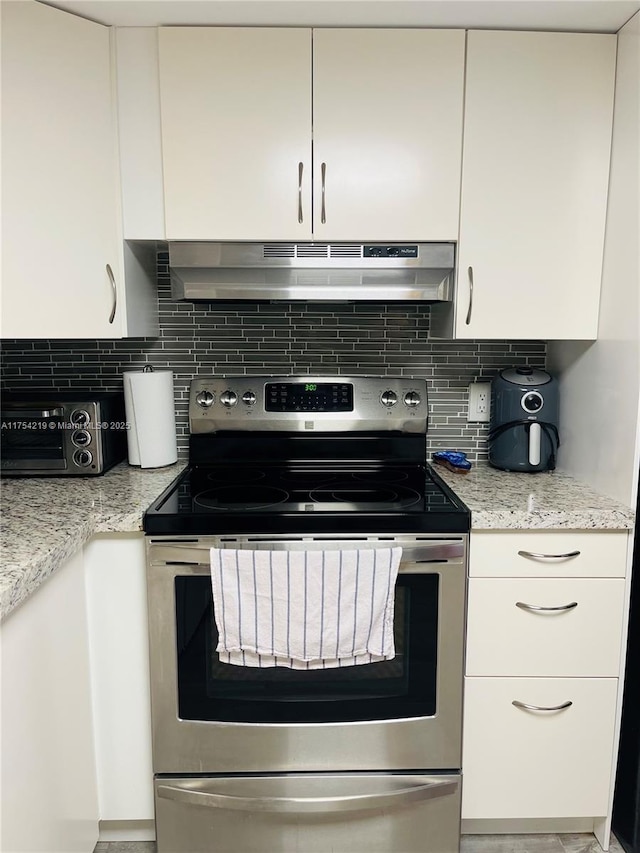 kitchen with under cabinet range hood, decorative backsplash, white cabinets, and stainless steel electric stove