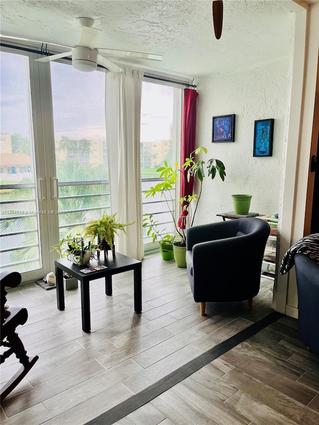 sitting room featuring a textured wall, ceiling fan, wood finished floors, a textured ceiling, and floor to ceiling windows