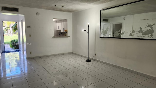 tiled empty room featuring baseboards, visible vents, and a textured ceiling