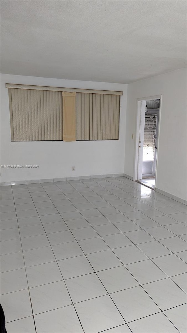 unfurnished room featuring light tile patterned floors, a textured ceiling, and baseboards