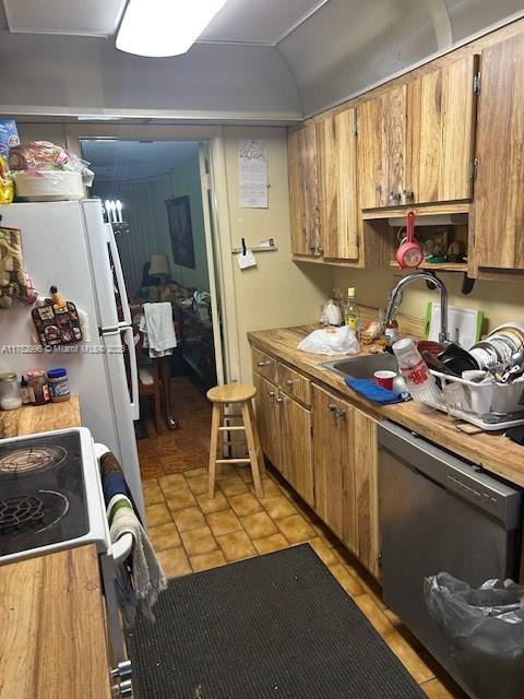 kitchen featuring dishwashing machine, a sink, vaulted ceiling, light countertops, and brown cabinetry