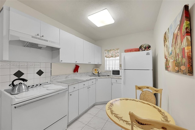 kitchen with white appliances, white cabinets, light countertops, under cabinet range hood, and a sink