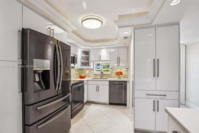 kitchen with stainless steel appliances, a raised ceiling, light countertops, backsplash, and white cabinetry