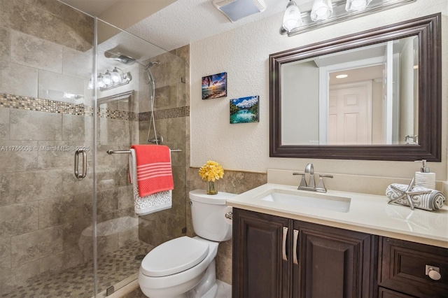 full bath featuring a textured wall, a shower stall, toilet, and vanity