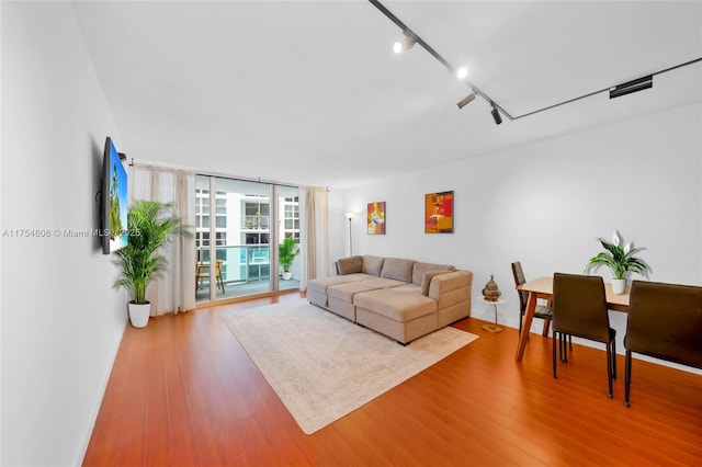 living area featuring rail lighting, expansive windows, baseboards, and wood finished floors