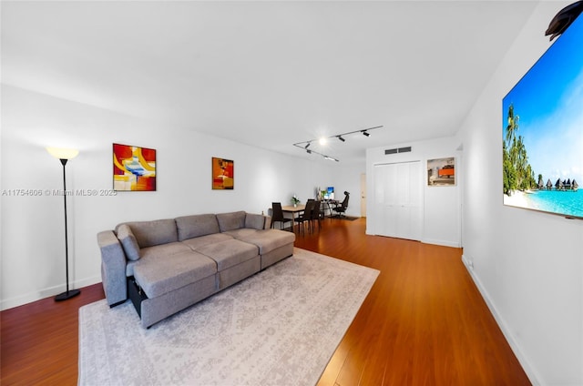 living room with rail lighting, visible vents, baseboards, and wood finished floors