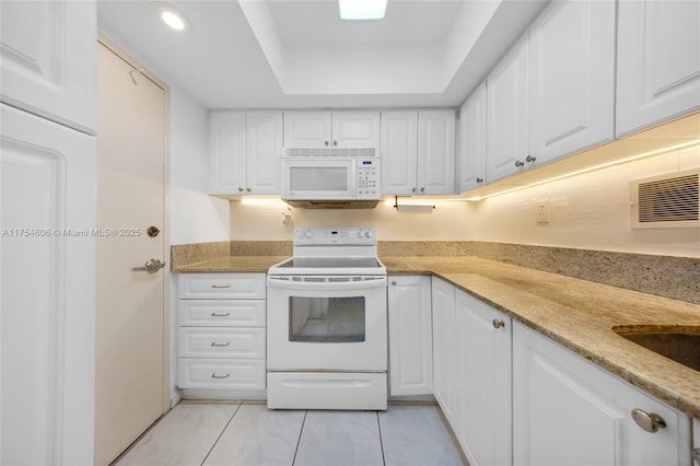 kitchen featuring light stone countertops, white appliances, a tray ceiling, and white cabinets