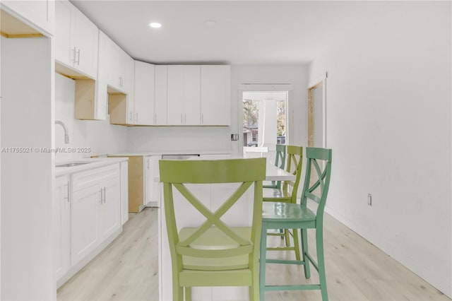 kitchen with light wood-type flooring, white cabinetry, and a sink