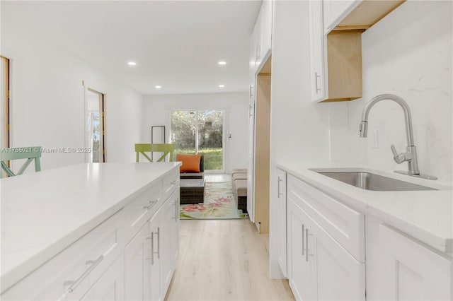 kitchen with white cabinets, light stone countertops, light wood finished floors, and a sink