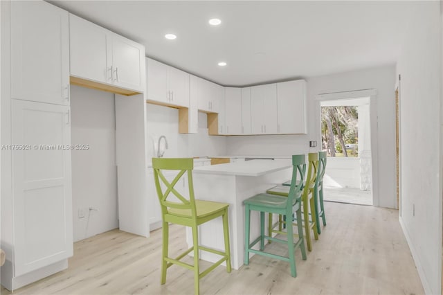 kitchen featuring a center island, recessed lighting, light wood-style flooring, white cabinets, and a kitchen bar