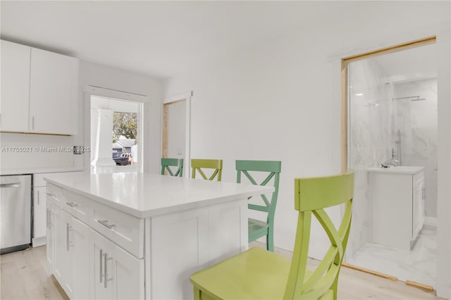 kitchen with light wood-style flooring, white cabinetry, light countertops, a center island, and dishwasher