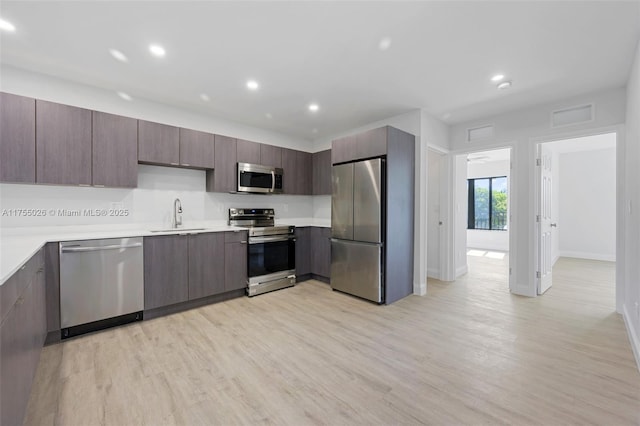 kitchen with stainless steel appliances, light wood-type flooring, light countertops, and a sink