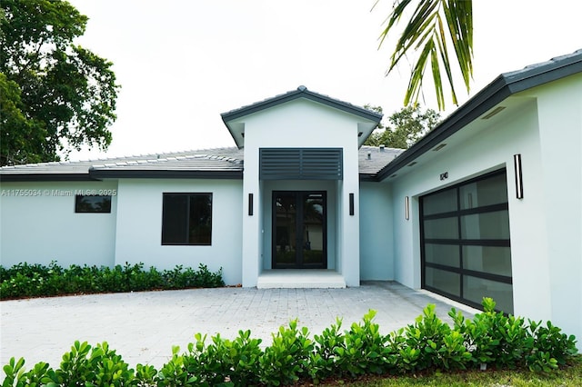 doorway to property with an attached garage, stucco siding, and french doors